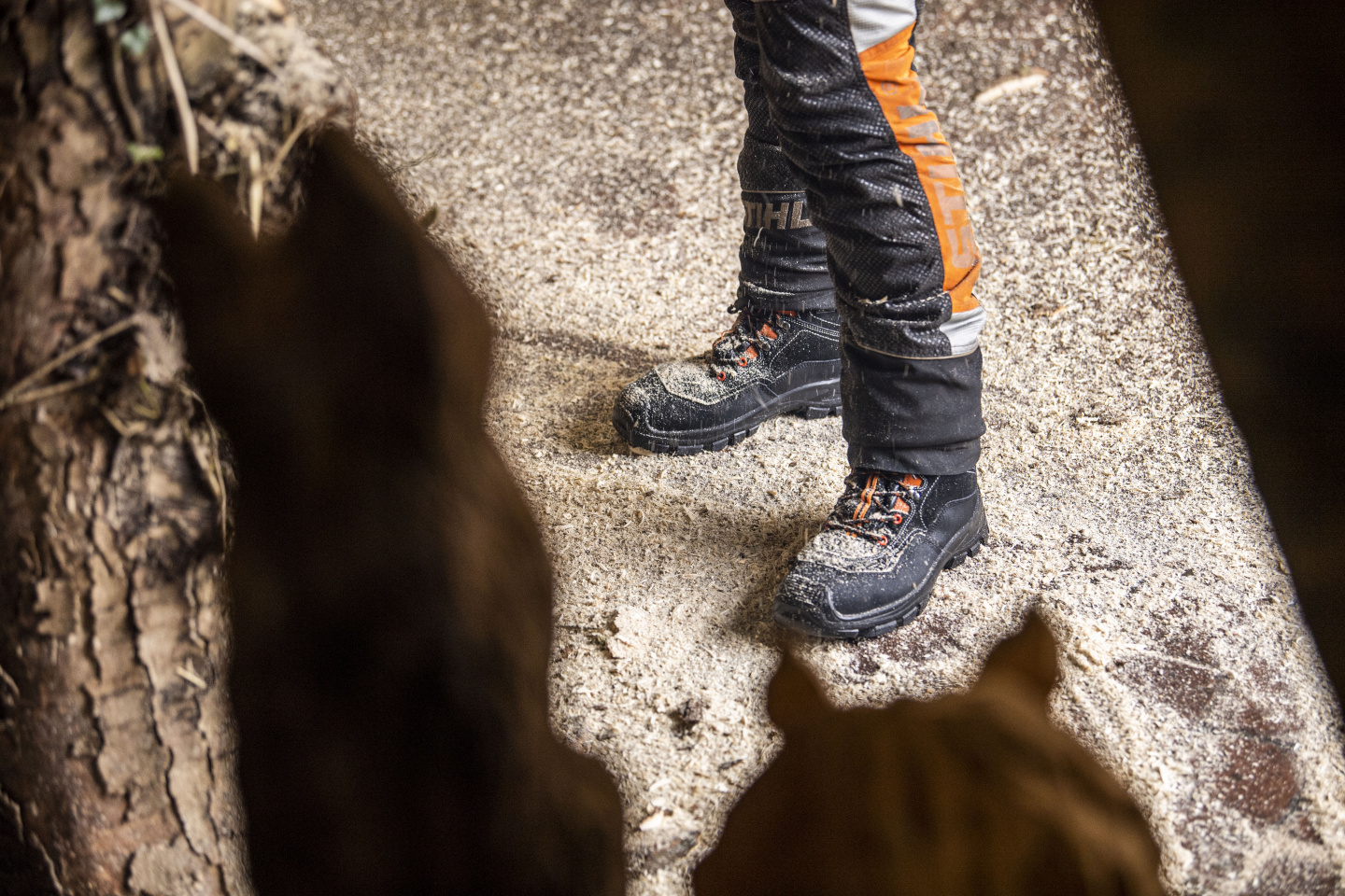 Blick auf Schnittschutzstiefel und Schnittschutzhose von oben in einer Holzkunstwerkstatt.