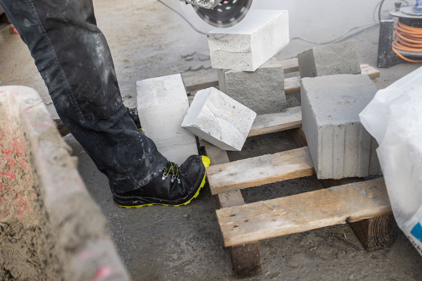 Steine werden auf einer Baustelle durchtrennt, ein Stück fällt in Richtung Schuhe.